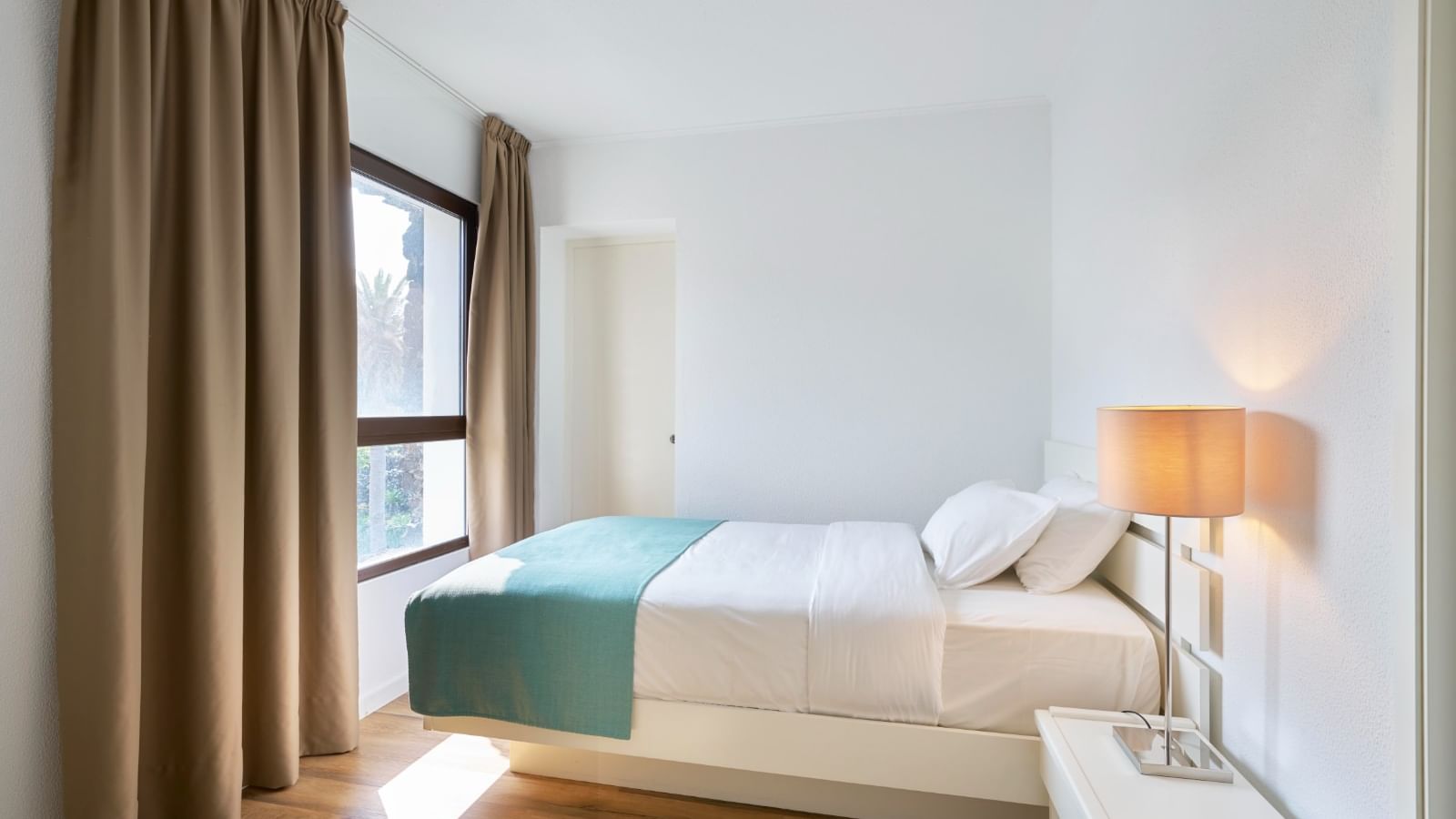 Nightstand by the cozy bed in the bright Suite with wooden flooring at Bensaude Hotels