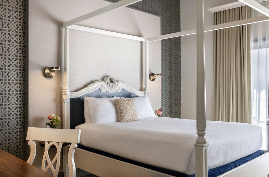 White four-poster bed by a carved desk chair under a grey patterned wall in Balcony Junior Suite at Warwick San Francisco