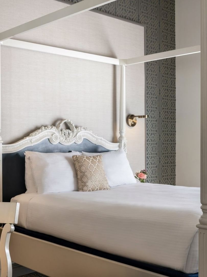 White four-poster bed by a carved desk chair under a grey patterned wall in Balcony Junior Suite at Warwick San Francisco