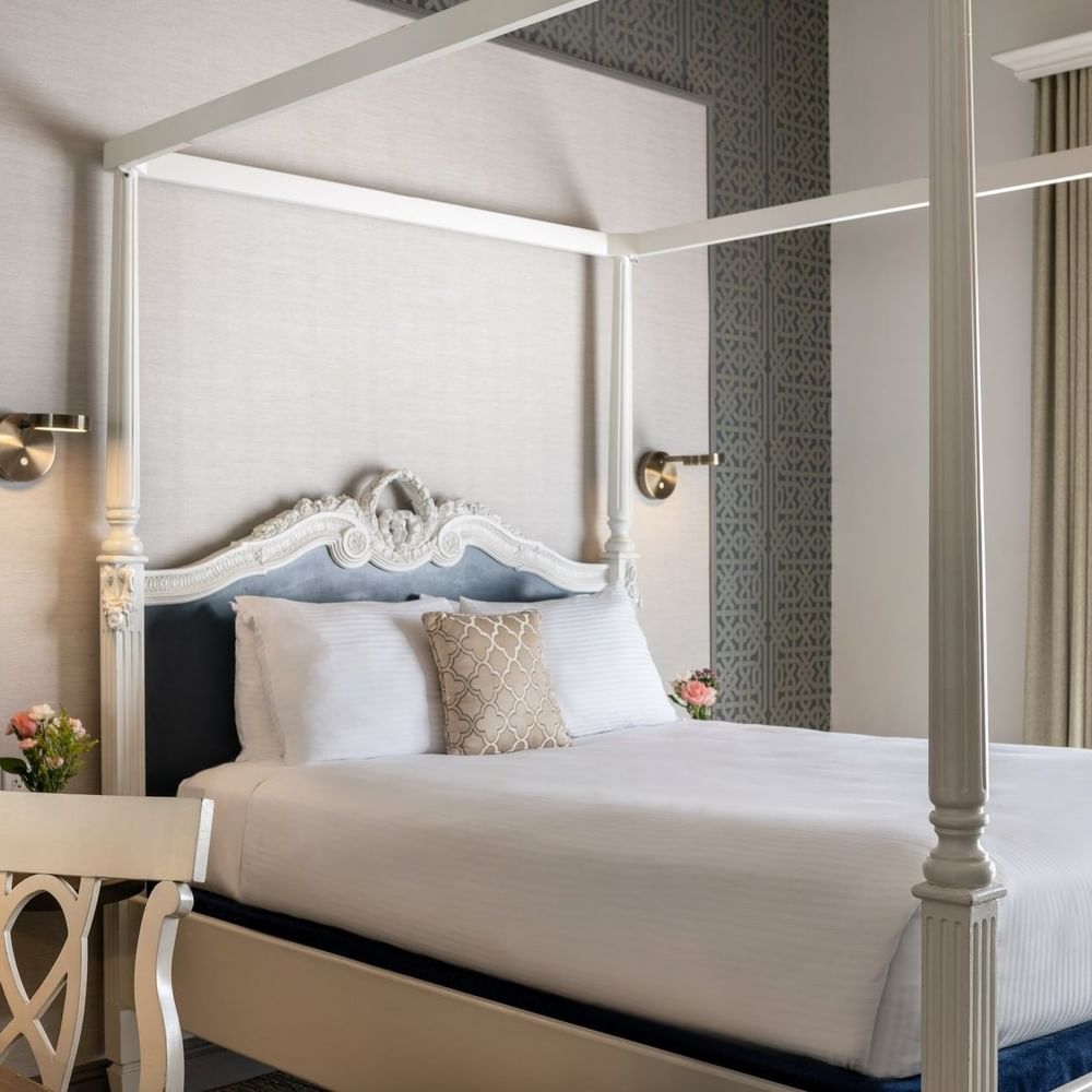 White four-poster bed by a carved desk chair under a grey patterned wall in Balcony Junior Suite at Warwick San Francisco
