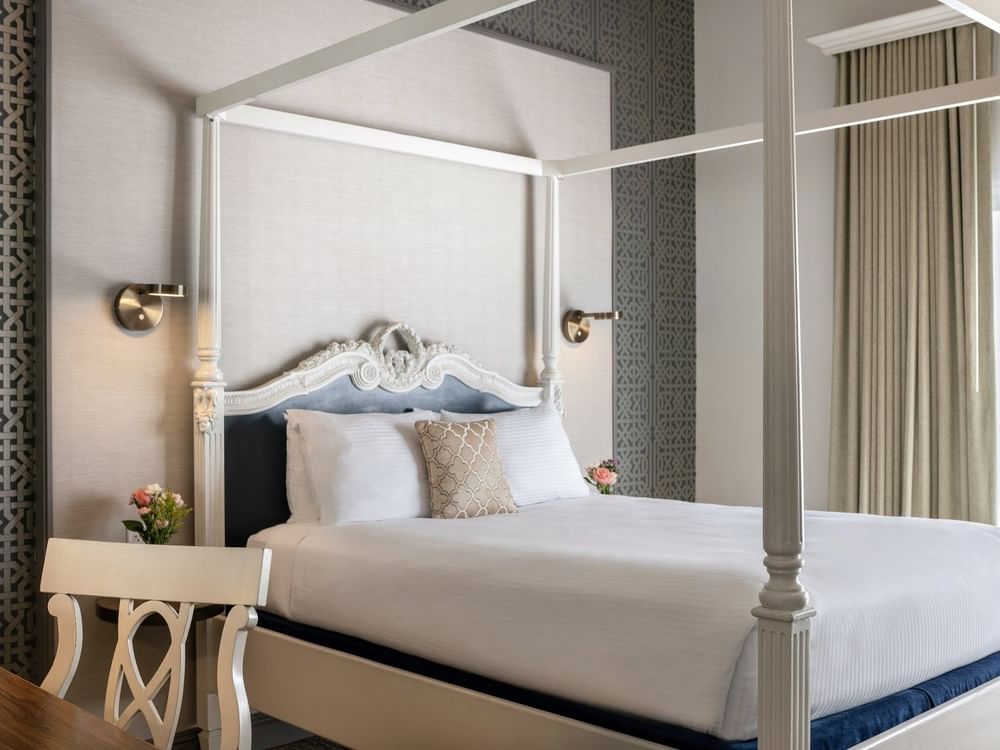 White four-poster bed by a carved desk chair under a grey patterned wall in Balcony Junior Suite at Warwick San Francisco