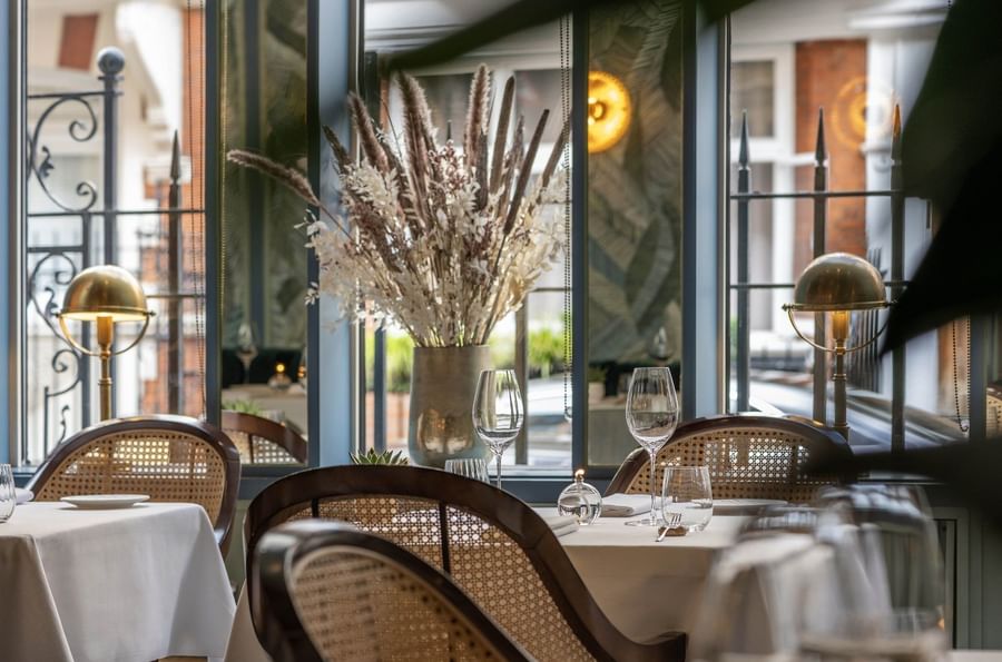 Dining tables set by cane chairs near large windows in the restaurant at The Capital Hotel, Apartments and Townhouse