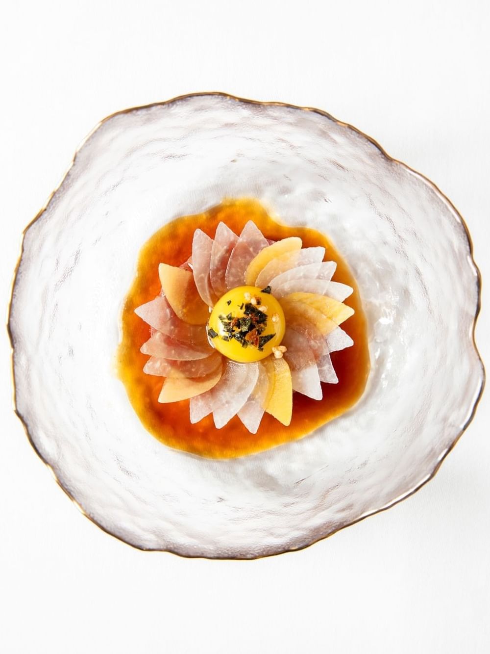 Sashimi dish arranged in a flower pattern with a golden yolk in a bowl at The Capital Hotel, Apartments and Townhouse