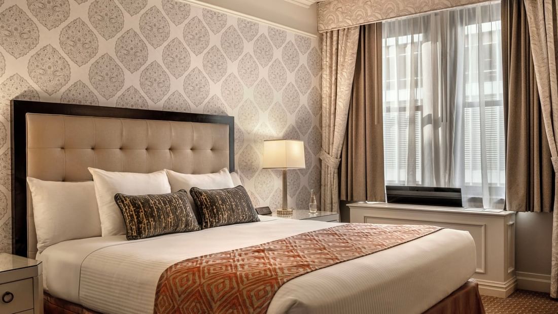 Close-up of bed with patterned pillows against decorative wallpaper in On The Avenue One Bedroom Suite at Warwick New York