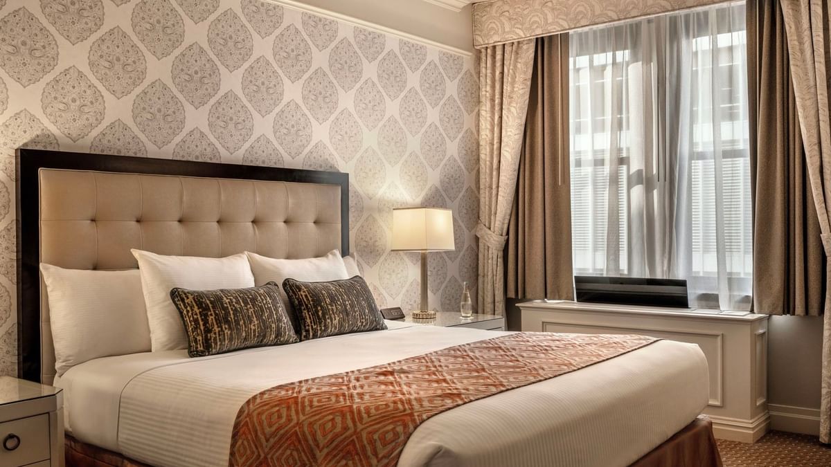 Close-up of bed with patterned pillows against decorative wallpaper in On The Avenue One Bedroom Suite at Warwick New York