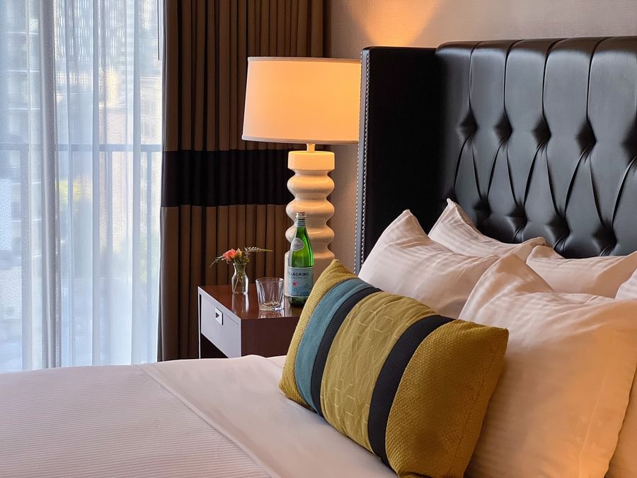 Teal and yellow pillows by a white lamp under a tufted black headboard in Emerald Suite at Warwick Seattle