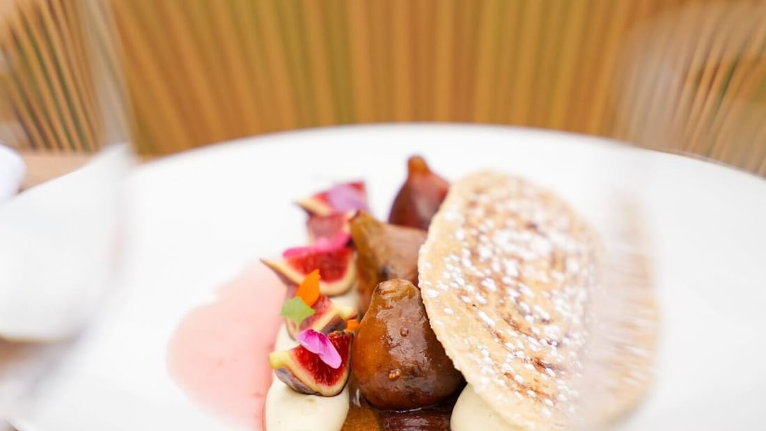 Plat élégant avec des figues, une sauce marron, une crêpe, et une décoration florale sur une table en bois.
