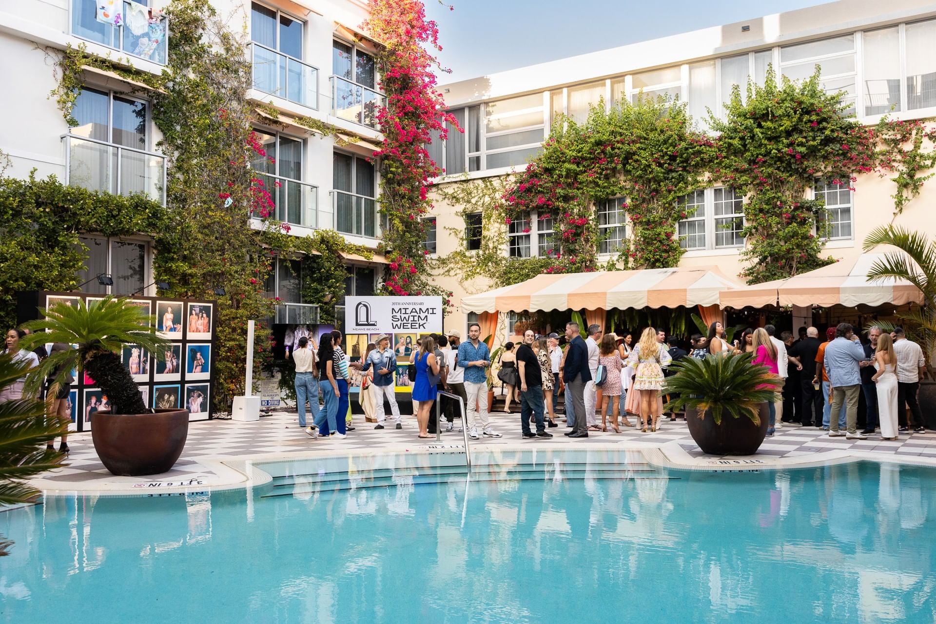 A group of people gathered around a pool in front of a building with plants and flowers.