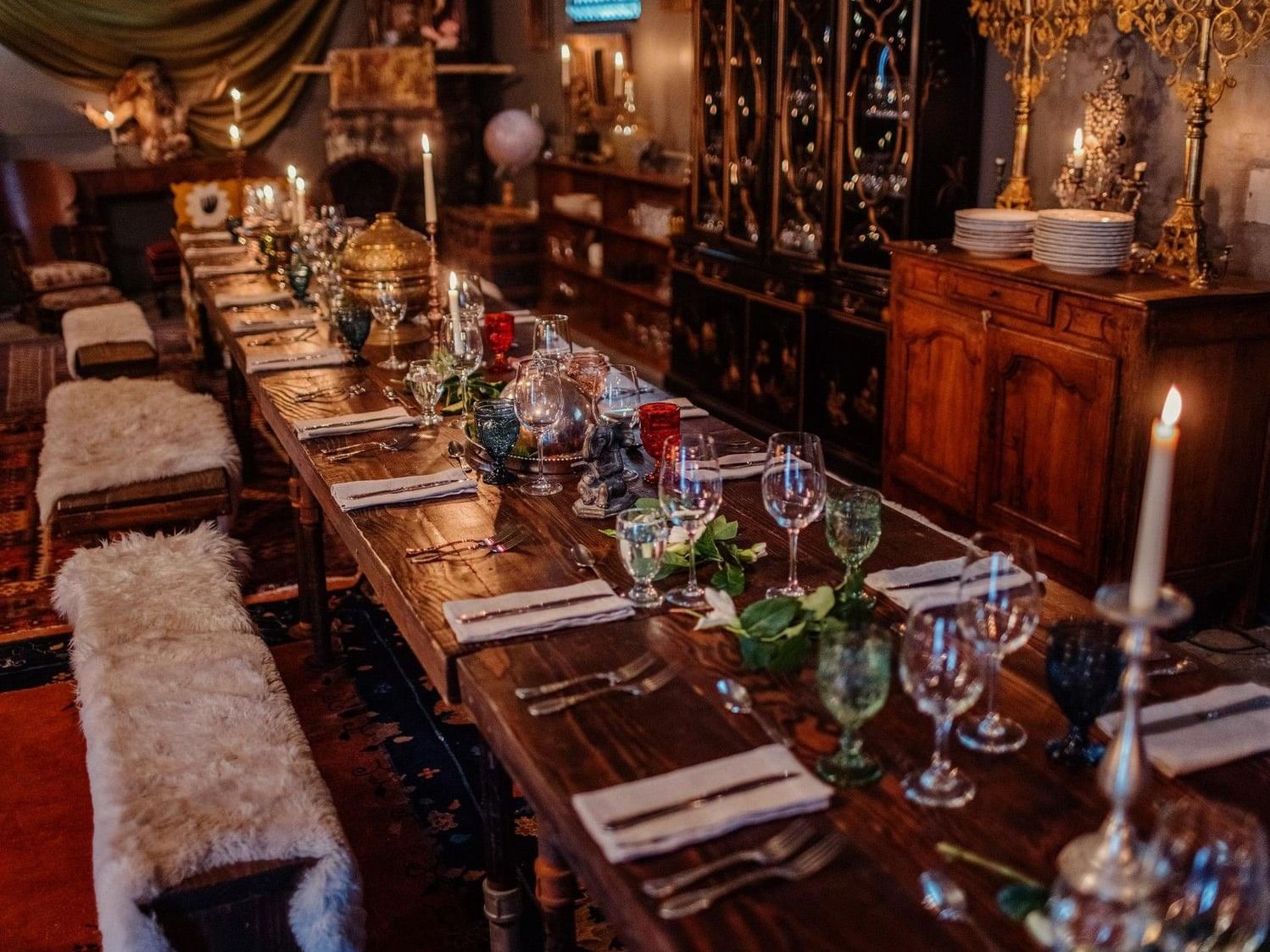 Long banquette table set with wine glasses by plush sheepskin benches under soft light in The Great Hall at Elsewhere Topanga