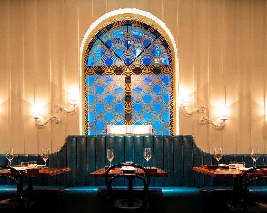 Ciaorigato Restaurant interior with a gold-patterned arch window, teal booths, and dining tables at Hotel Bijou