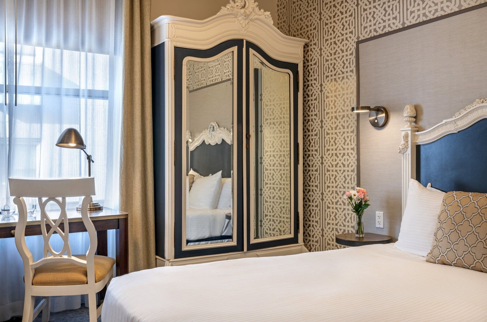 Large armoire by a white desk chair and bed under a patterned wallpaper in Superior Queen Room at Warwick San Francisco
