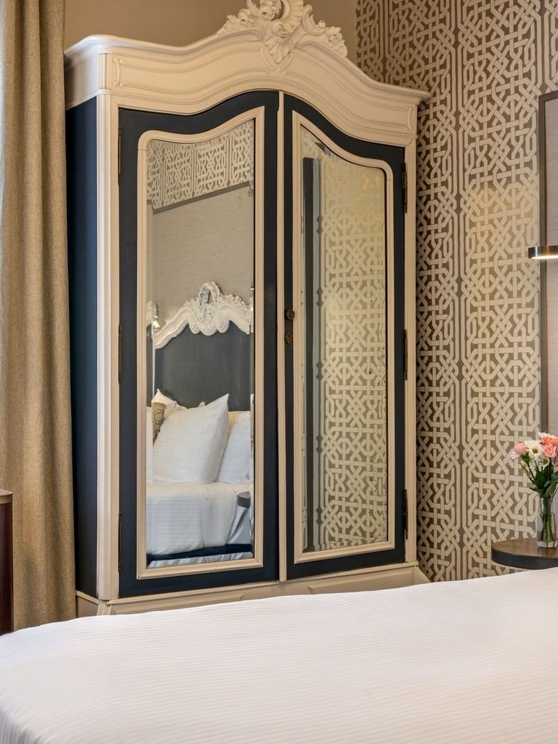 Large armoire by a white desk chair and bed under a patterned wallpaper in Superior Queen Room at Warwick San Francisco