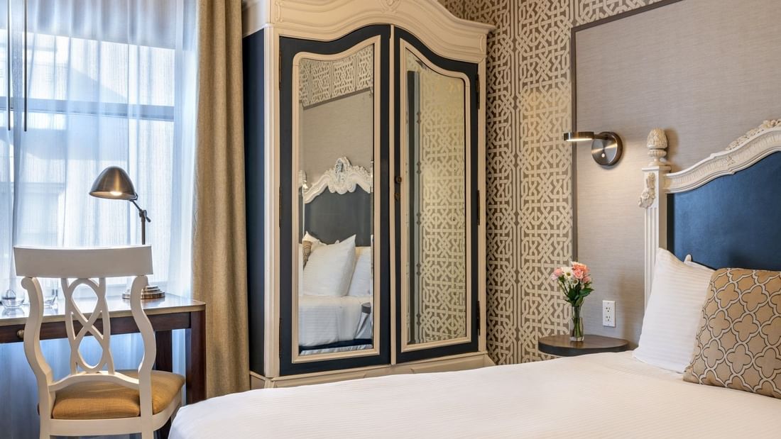 Large armoire by a white desk chair and bed under a patterned wallpaper in Superior Queen Room at Warwick San Francisco
