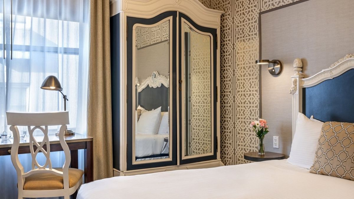 Large armoire by a white desk chair and bed under a patterned wallpaper in Superior Queen Room at Warwick San Francisco