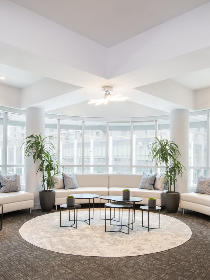 White sofas placed by small round tables on a circular rug in Salon Lounge at Warwick Le Crystal Montreal