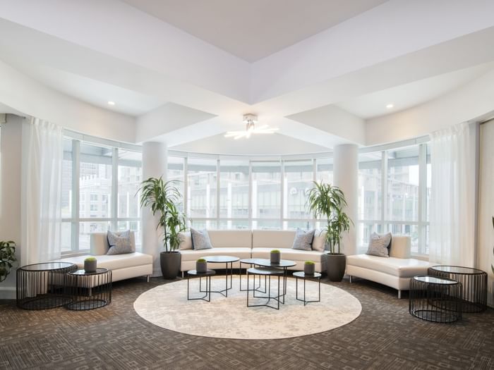 White sofas placed by small round tables on a circular rug in Salon Lounge at Warwick Le Crystal Montreal
