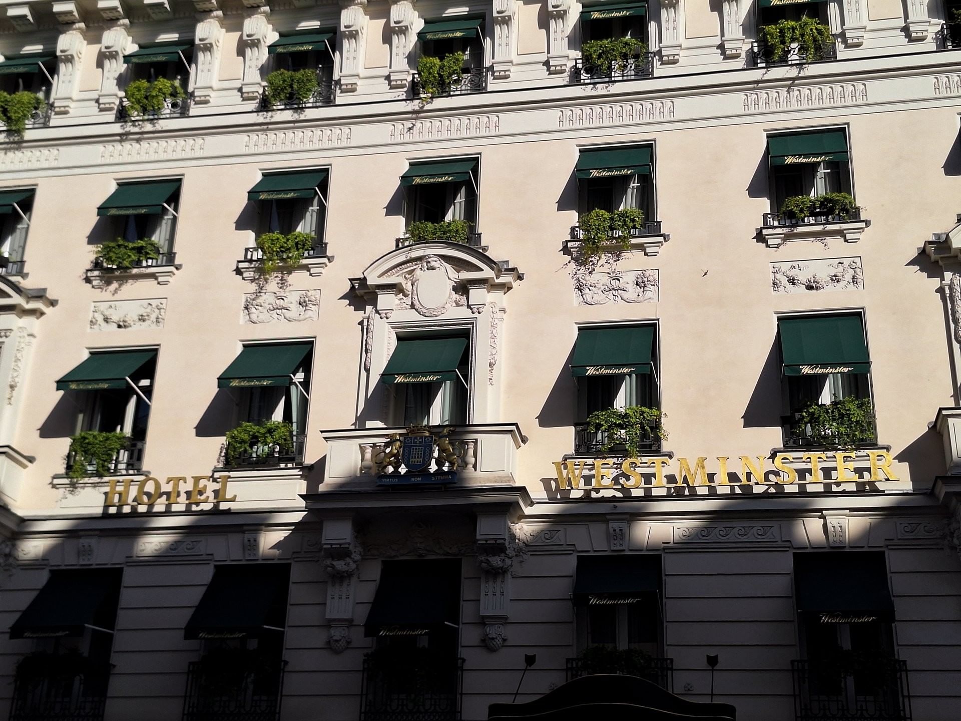 Exterior facade with green awnings and lush plants at Hotel Westminster Paris, featuring gold signage by the stone wall
