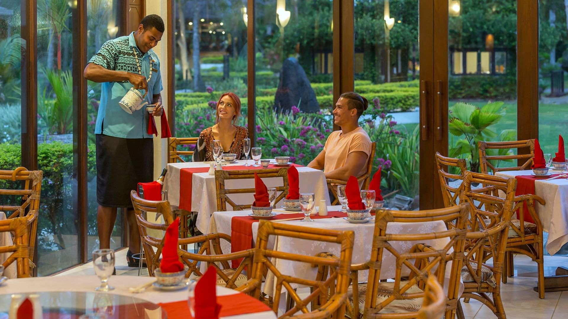 Waiter serving a couple at a table by large glass doors under warm light in Bamboo Terrace at The Naviti Resort - Fiji