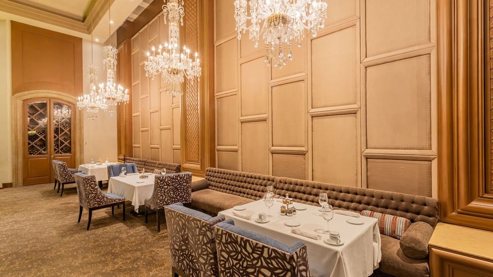 Formal dining room in Tierra Mía with a long tufted bench, wood paneled walls, and crystal lamps at Quinta Real Monterrey