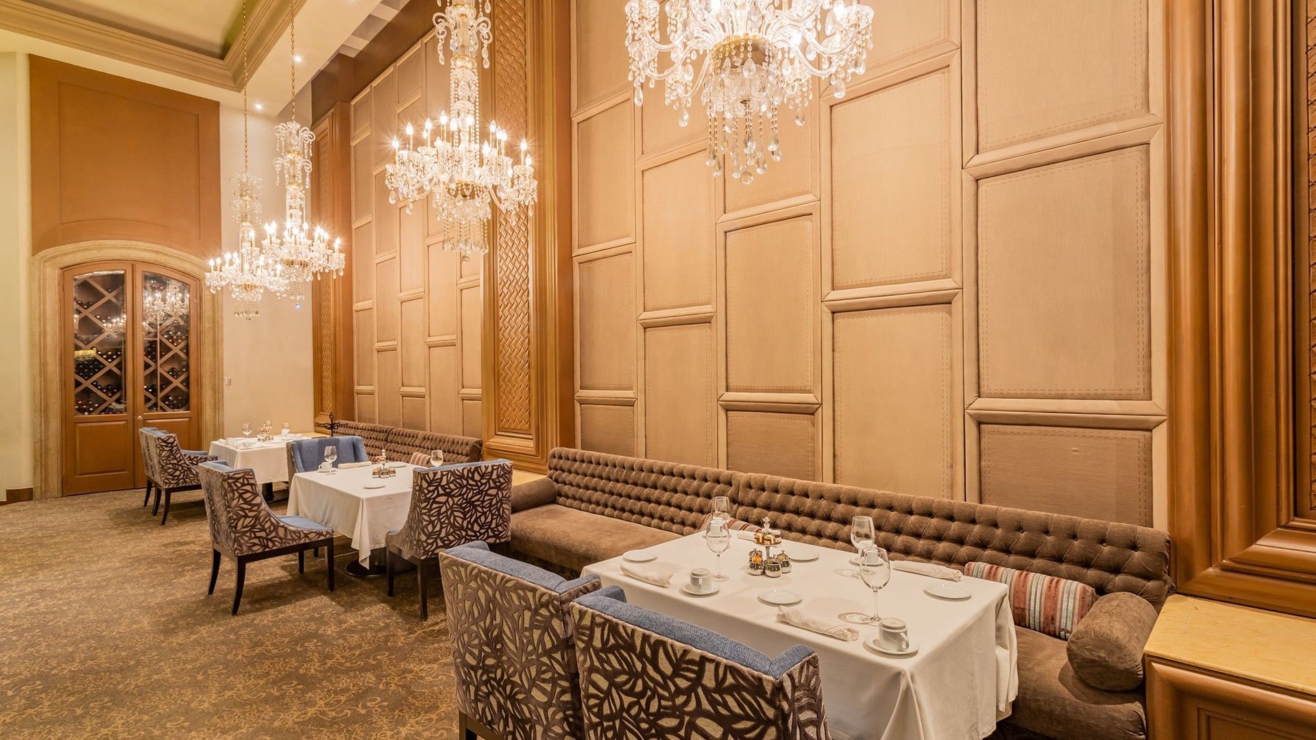 Formal dining room in Tierra Mía with a long tufted bench, wood paneled walls, and crystal lamps at Quinta Real Monterrey