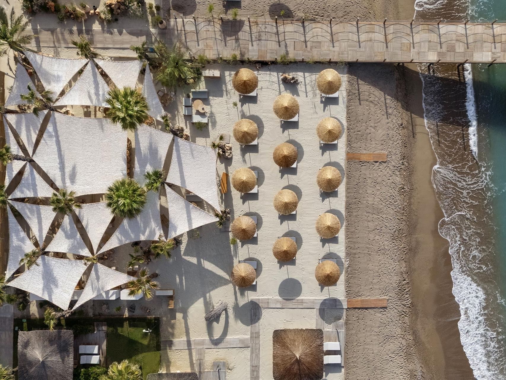 Aerial view of a beach resort with a white canopy, thatched umbrellas, and ocean waves Cullinan Belek.