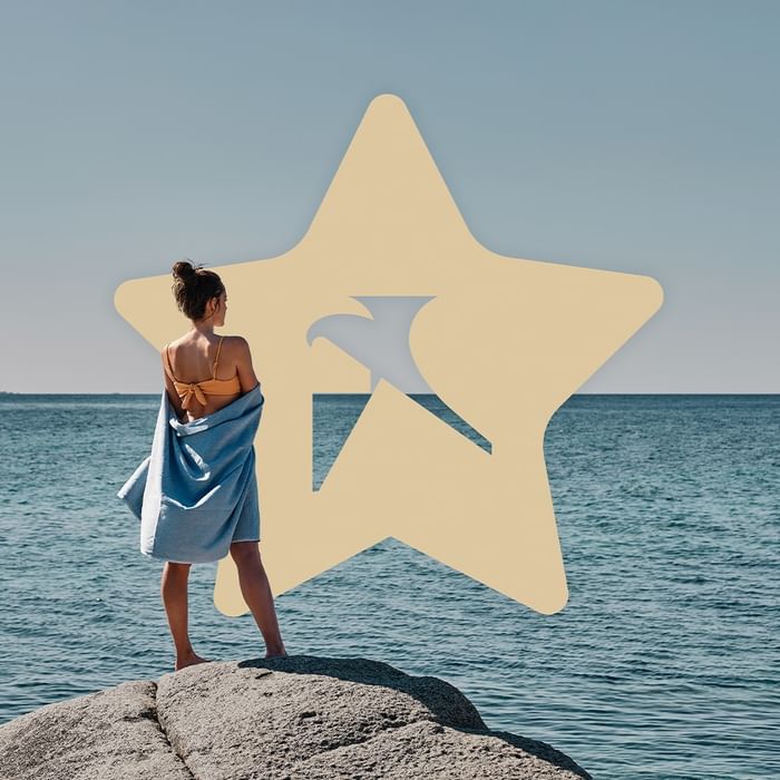 Donna in costume da bagno e asciugamano che guarda l'oceano con una stella dorata trasparente sopra di lei.