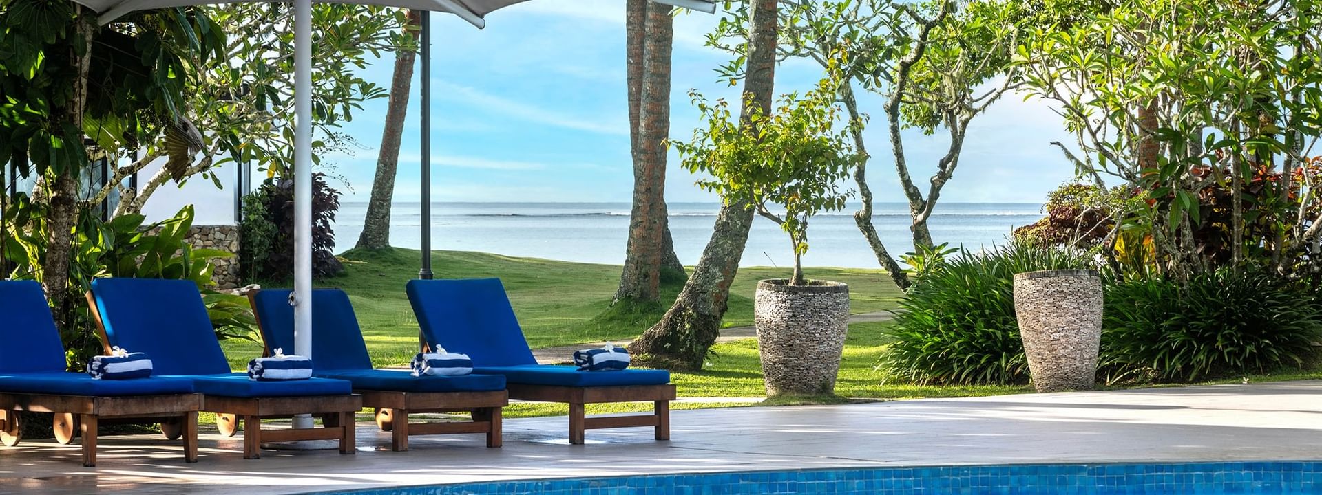 Poolside loungers under umbrella with ocean view at The Naviti Resort in Korolevu