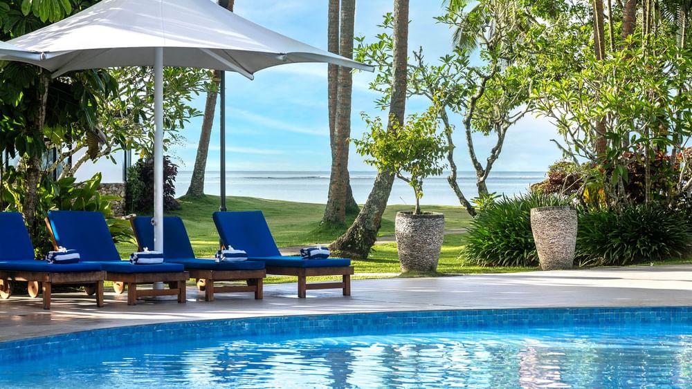 Poolside loungers under umbrella with ocean view at The Naviti Resort in Korolevu.