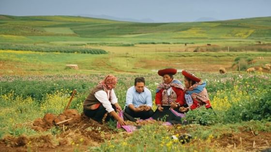 Four people in traditional Andean clothing gather around plants in a field with green hills at Sumaq Machu Picchu Hotel