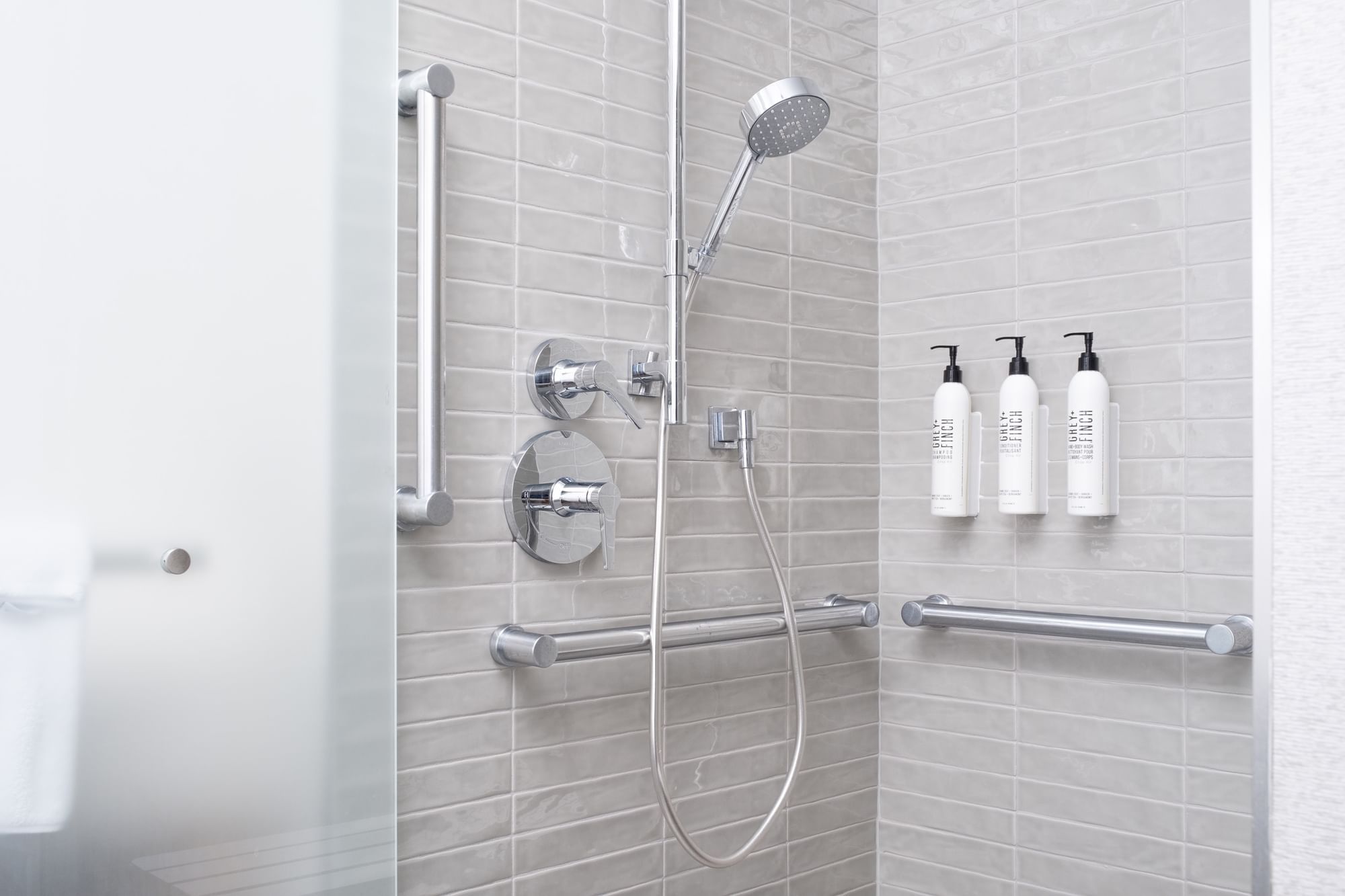 A modern bathroom shower with grab bars, a shower head, and soap bottles.