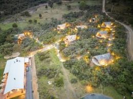 Aerial night view of illuminated glamping cabins along glowing paths in the forest at Casa Selvaggio