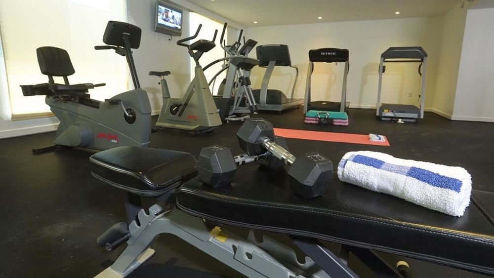 Dumbbells and a rolled towel on a weight bench by treadmills in the Fitness Centre at Warwick Paradise Island Bahamas