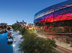 Shaw Centre by a canal, reflecting city lights, with historic architecture in the background, near ReStays Ottawa