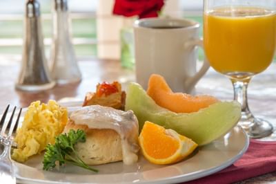 Breakfast plate with a biscuit and gravy, eggs, fruit and orange