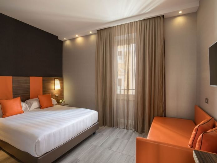 Deluxe Room featuring a double bed with orange pillows, a small sofa, a TV, and curtains at The Republic Hotel