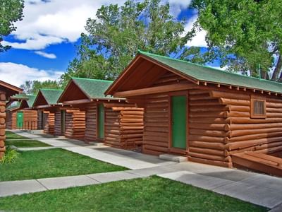 Log cabins with green roofs and vibrant green doors, lined up with a pathway at Buffalo Bill Village