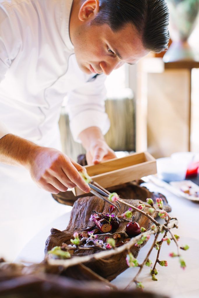 Chef preparing a meat dish surrounded by various ingredients and utensils at Umstead Hotel and Spa