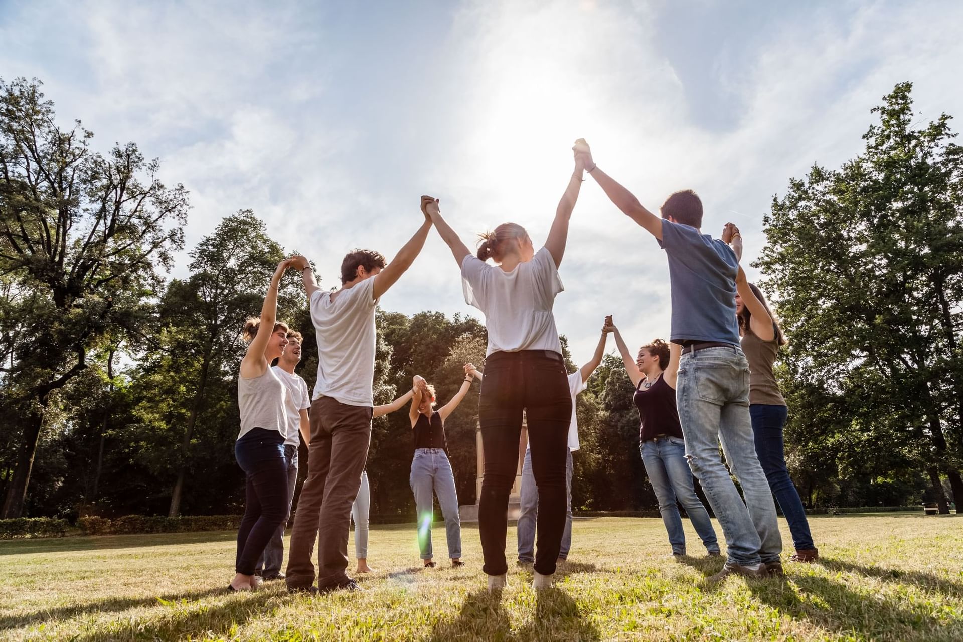 Group of people standing in a circle, raising their arms towards the sun on a green field at Las Dunas Resort Ica
