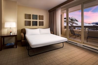 Cozy hotel room with a bed, chair, and balcony overlooking snowy mountains at Elevation Resort Spa