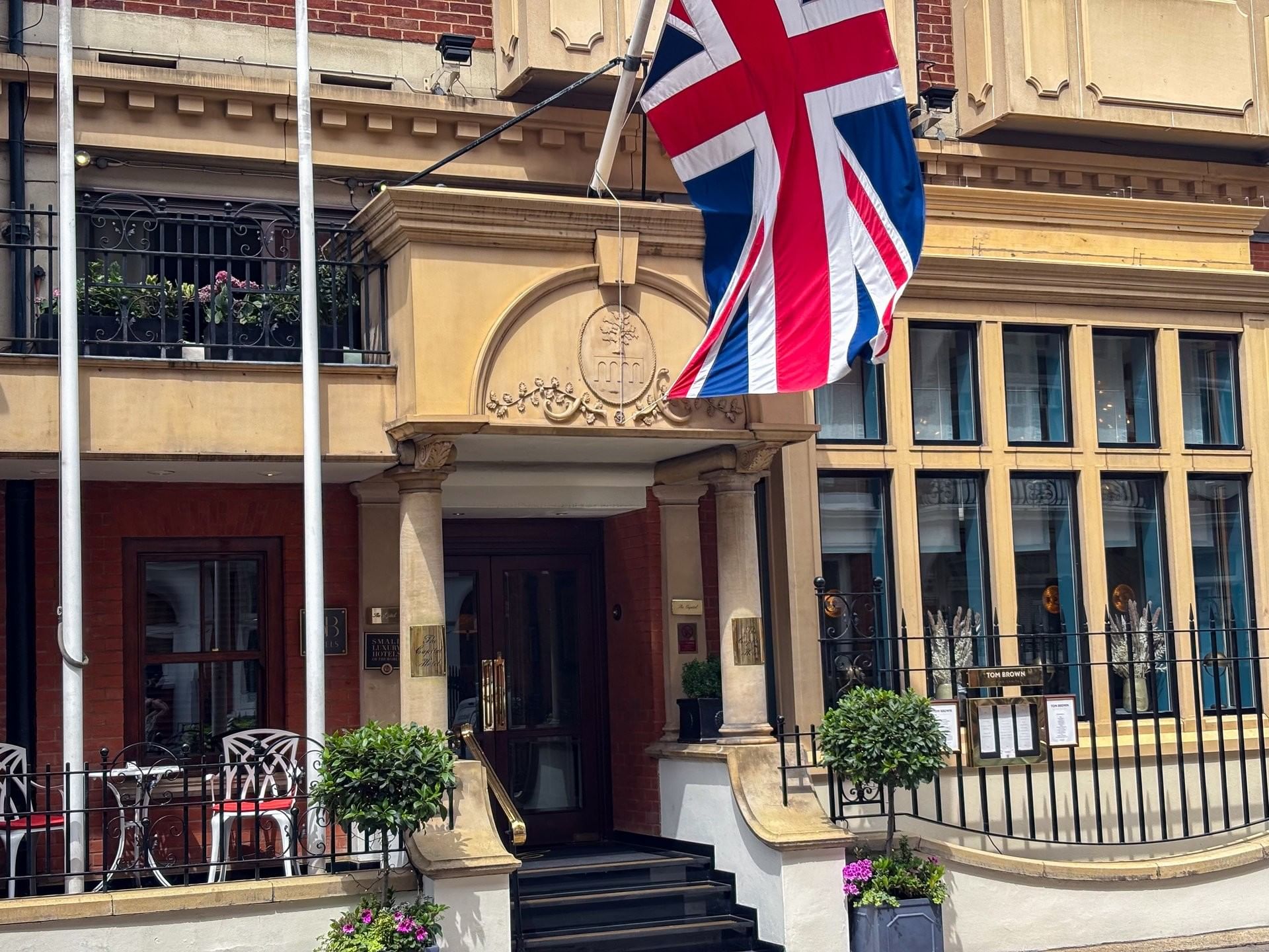 Front exterior of The Capital Hotel, Apartments and Townhouse with a British flag waving under a blue sky
