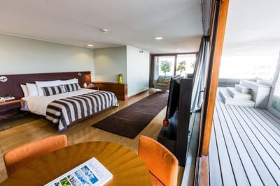 Cama a rayas junto a TV y mesa bajo luces empotradas con salida a terraza en Cosmopolitan Suite de NOI Vitacura