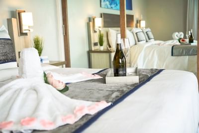 Wine on tray with swan towels and rose petals on plush white bed in Ocean View King at The Abidah Hotel by Accra