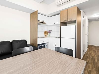 Modern kitchen and living area with a wooden table, black couches, and white appliances