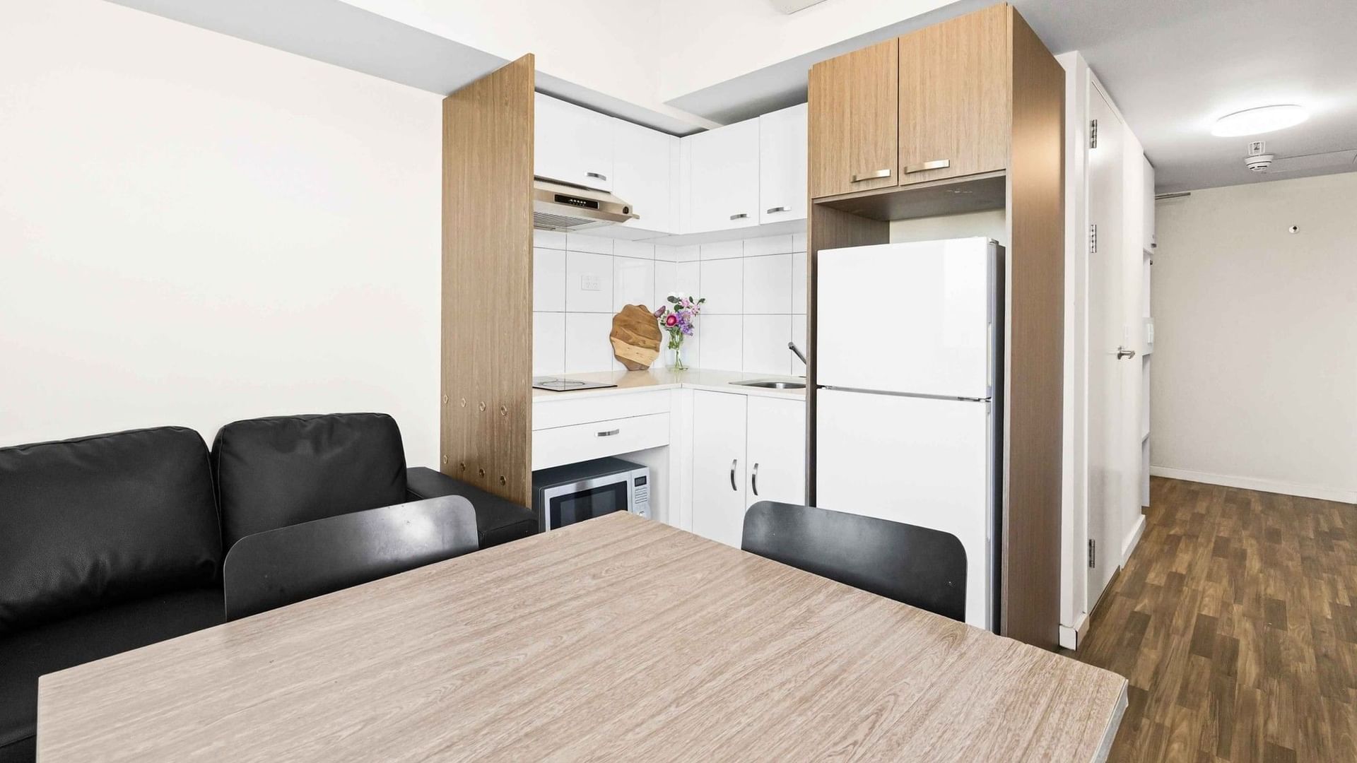 Modern kitchen and living area with a wooden table, black couches, and white appliances