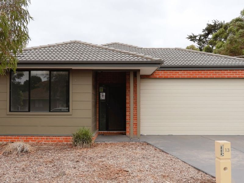Modern brick house with garage, driveway, and number 13 post, surrounded by greenery.