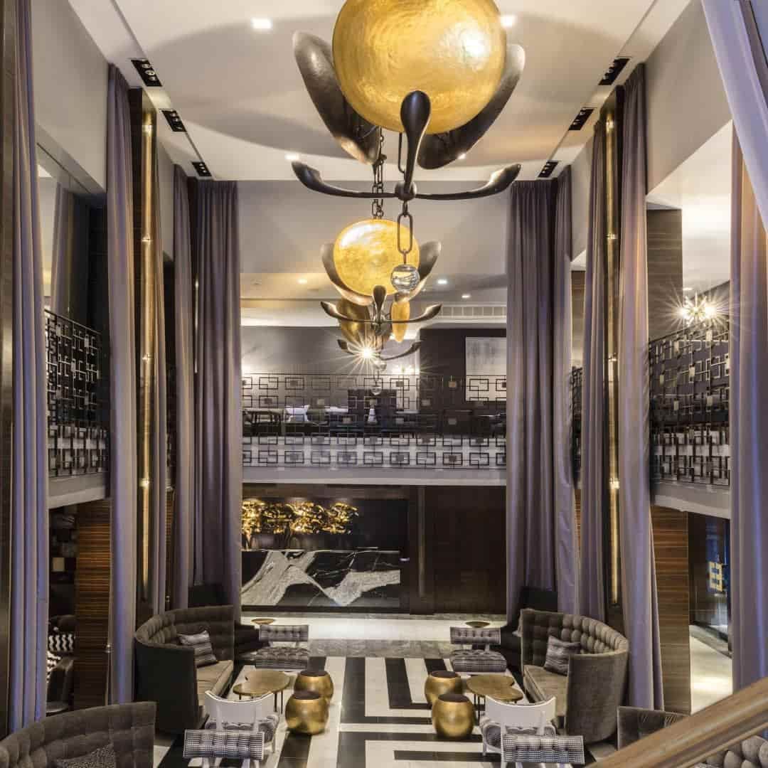 A luxurious hotel lobby with a high ceiling, chandelier, and modern furniture.