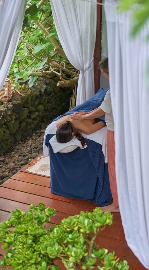 Guest receiving a relaxing massage treatment on an outdoor wooden deck surrounded by curtains at Caloura Hotel Resort