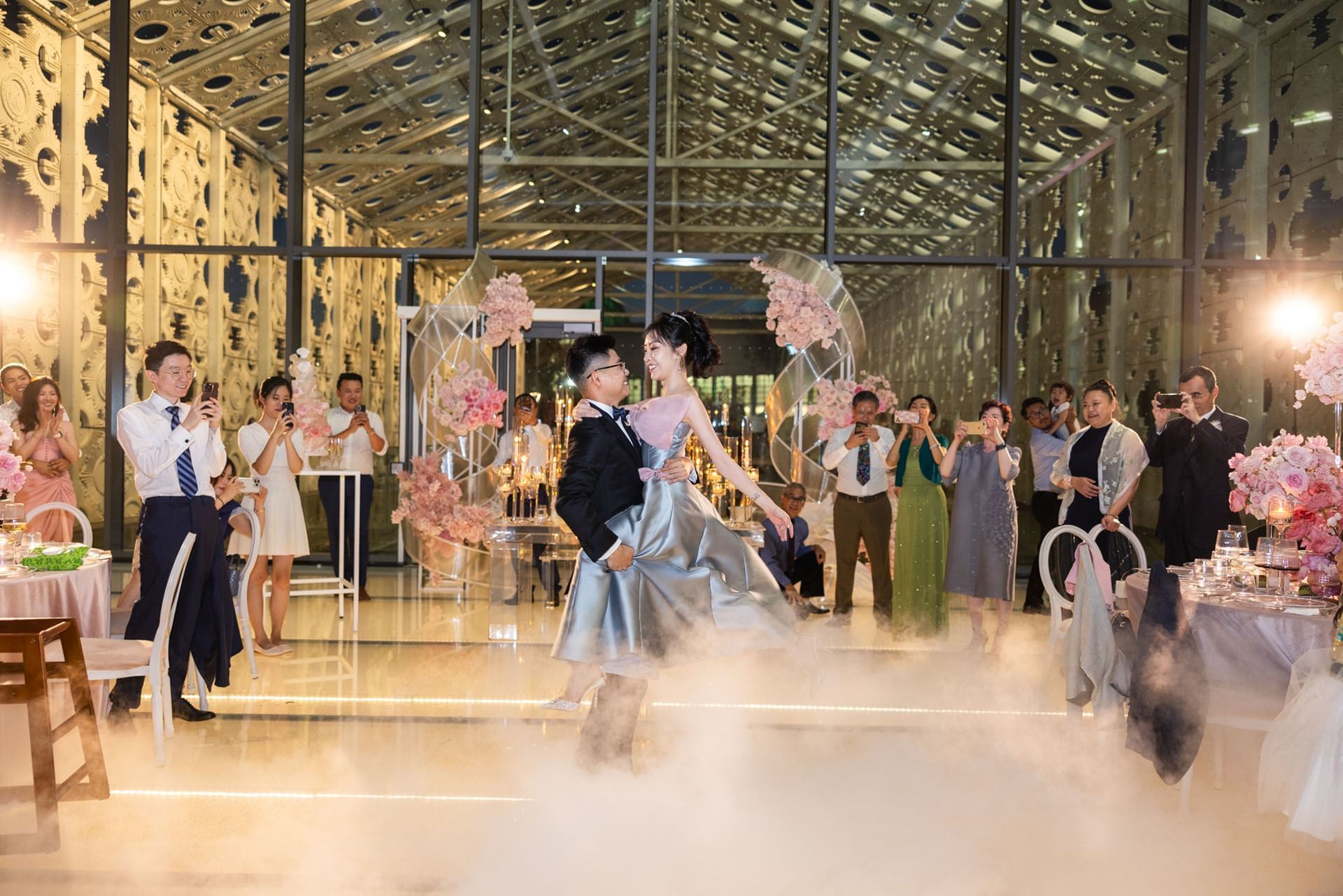Bride and groom dancing on a foggy floor by guests taking photos, under a glass pavilion roof near the Hotel X Toronto