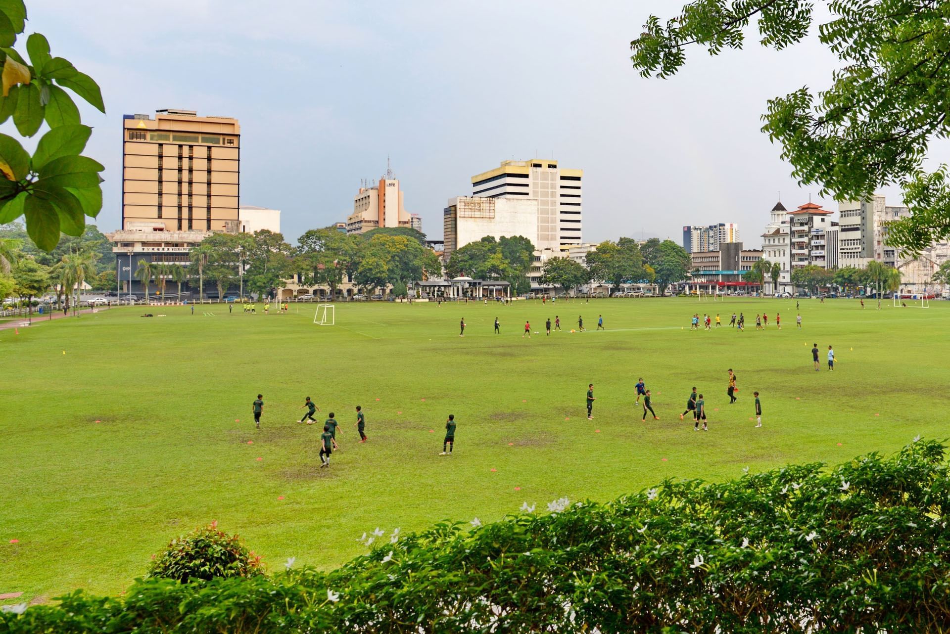 A green urban park with people playing soccer and Cititel Express Ipoh in the background