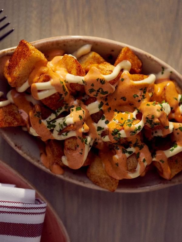 Crispy potatoes with spicy sauce & a bowl by a fork on a wooden table in In-Room Dining at Warwick San Francisco